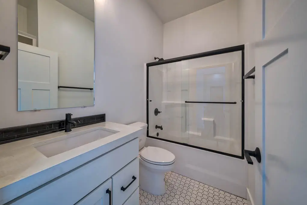Interior photo of a home built by Harvell Homes in Powell, Wyoming featuring a modern black and white farmhouse bathroom with sliding door bathtub shower, sink, and tile flooring