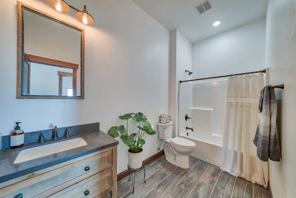 Interior photo of a home built by Harvell Homes in Powell, Wyoming featuring a modern black and white farmhouse bathroom with bathtub shower, sink, and wood-look plank tile flooring