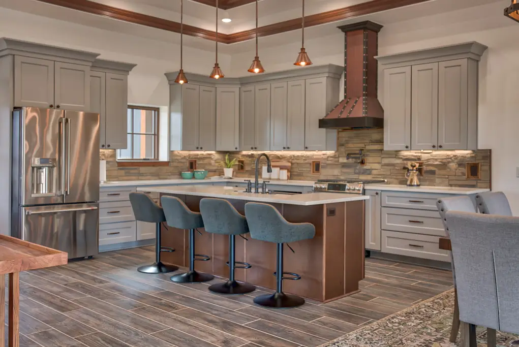 Interior photo of a home built by Harvell Homes in Powell, Wyoming featuring a luxurious custom kitchen with tray ceiling, premium appliances, wood island with premium countertop, wall-mount pot filler faucet, farmhouse kitchen sink, elevated stone backsplash, kitchen hood and wood-look plank tile flooring