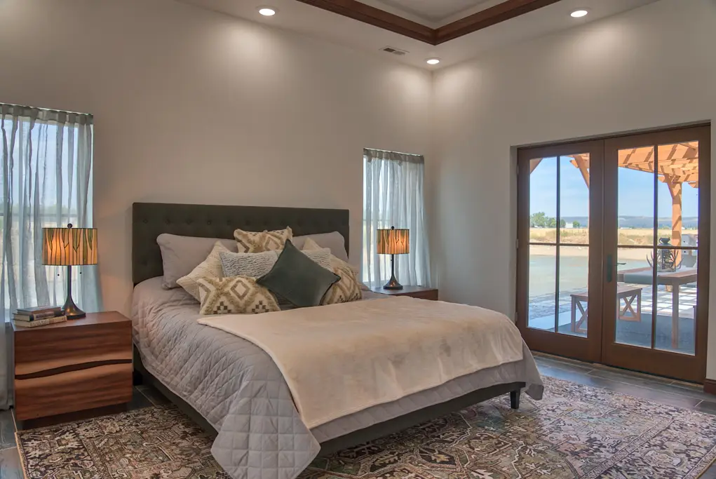 Interior photo of a home built by Harvell Homes in Powell, Wyoming featuring a luxurious and furnished bedroom with tray ceiling, balcony double french doors, and wood-look plank tile flooring