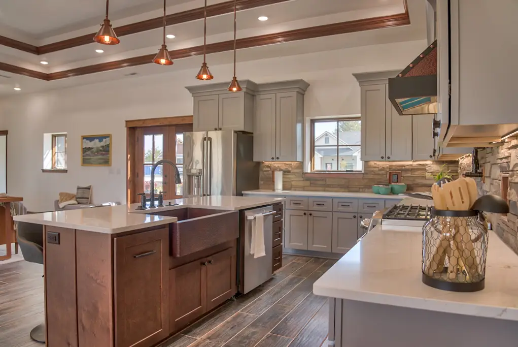 Interior photo of a furnished home built by Harvell Homes in Powell, Wyoming featuring an open-floor dining room and luxurious custom kitchen with tray ceiling, premium appliances, wood island with premium countertop, wall-mount pot filler faucet, farmhouse kitchen sink, and elevated stone backsplash