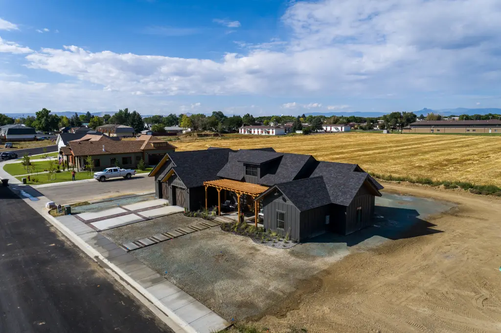 Exterior angled drone photo of a one-story modern black home built by Harvell Homes in Powell, Wyoming featuring front yard with pergola and custom driveway
