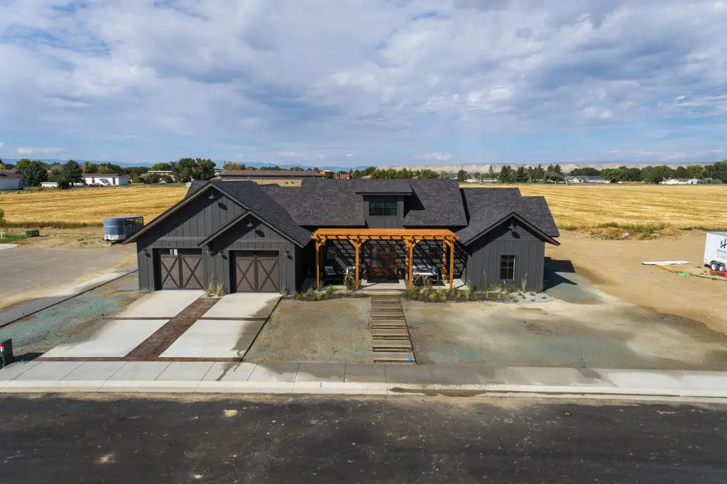 Exterior drone photo of a one-story modern black home built by Harvell Homes in Powell, Wyoming featuring front yard with pergola and custom driveway