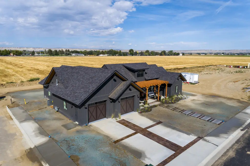 Exterior angled drone photo of a one-story modern black home built by Harvell Homes in Powell, Wyoming featuring front yard with pergola and custom driveway
