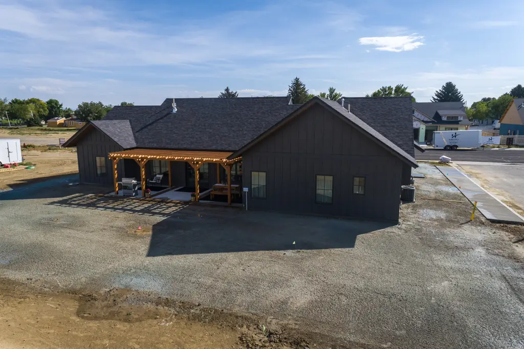 Exterior drone photo of a one-story modern black home built by Harvell Homes in Powell, Wyoming featuring pergola and in-progress backyard landscaping