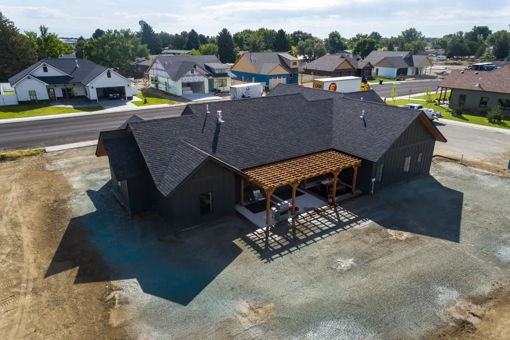 Exterior drone photo of a one-story modern black home built by Harvell Homes in Powell, Wyoming featuring pergola and in-progress backyard landscaping