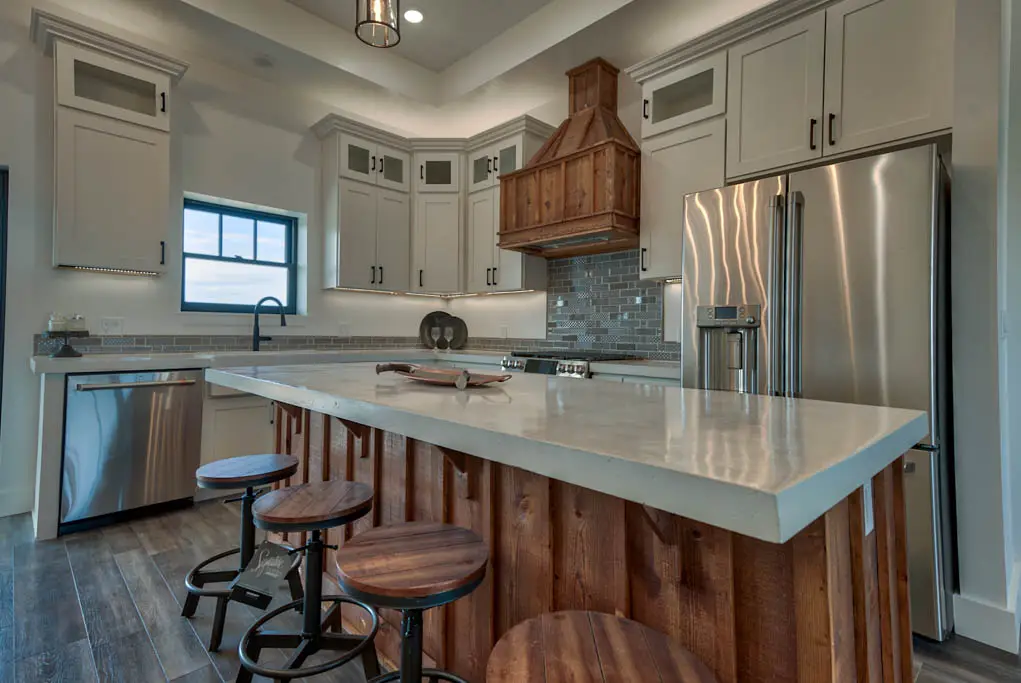 Interior photo of a home built by Harvell Homes in Powell, Wyoming featuring a luxurious custom kitchen with premium appliances, wood island with premium countertop, farmhouse kitchen sink, elevated backsplash, and wood vent kitchen hood