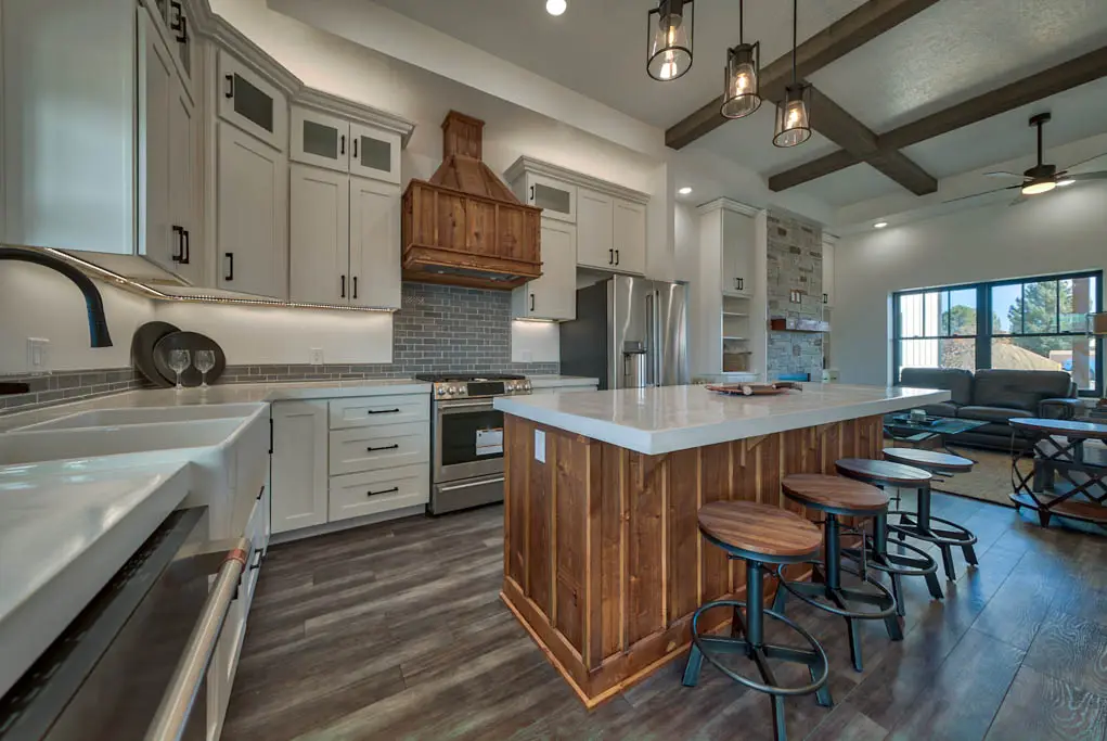 Interior photo of a home built by Harvell Homes in Powell, Wyoming featuring a luxurious open-floor living room and custom kitchen with premium appliances, wood island with premium countertop, farmhouse kitchen sink, elevated backsplash, and wood vent kitchen hood