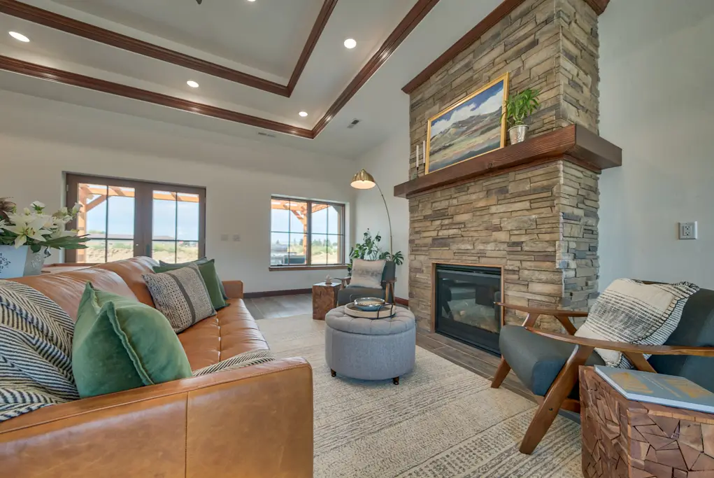 Interior photo of a home built by Harvell Homes in Powell, Wyoming featuring a furnished living room with tray ceiling and floor-to-ceiling stone fireplace