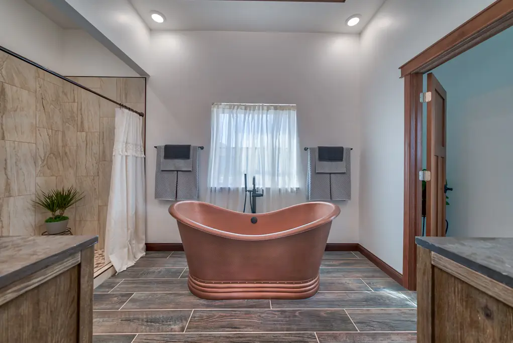 Interior photo of a home built by Harvell Homes in Powell, Wyoming featuring a luxurious bathroom with shower, freestanding tub, and wood-plank tile flooring