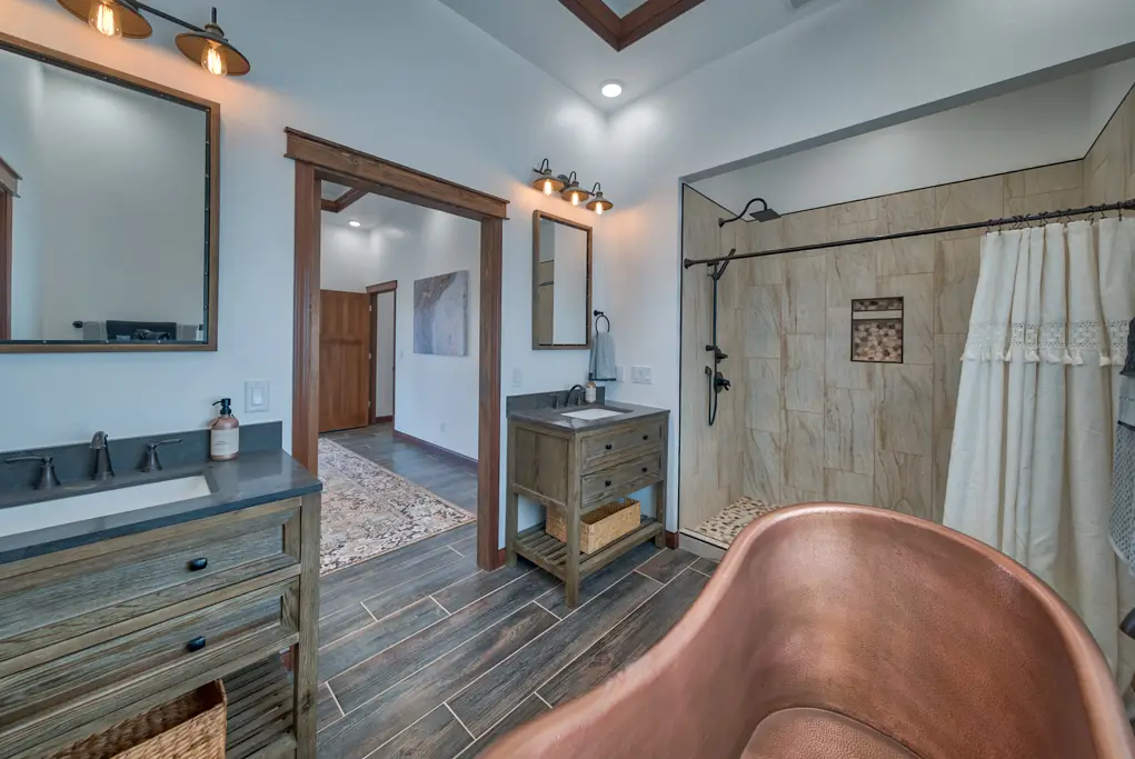 Interior photo of a home built by Harvell Homes in Powell, Wyoming featuring a luxurious bathroom with shower, freestanding tub, wood-plank tile flooring, and double sinks