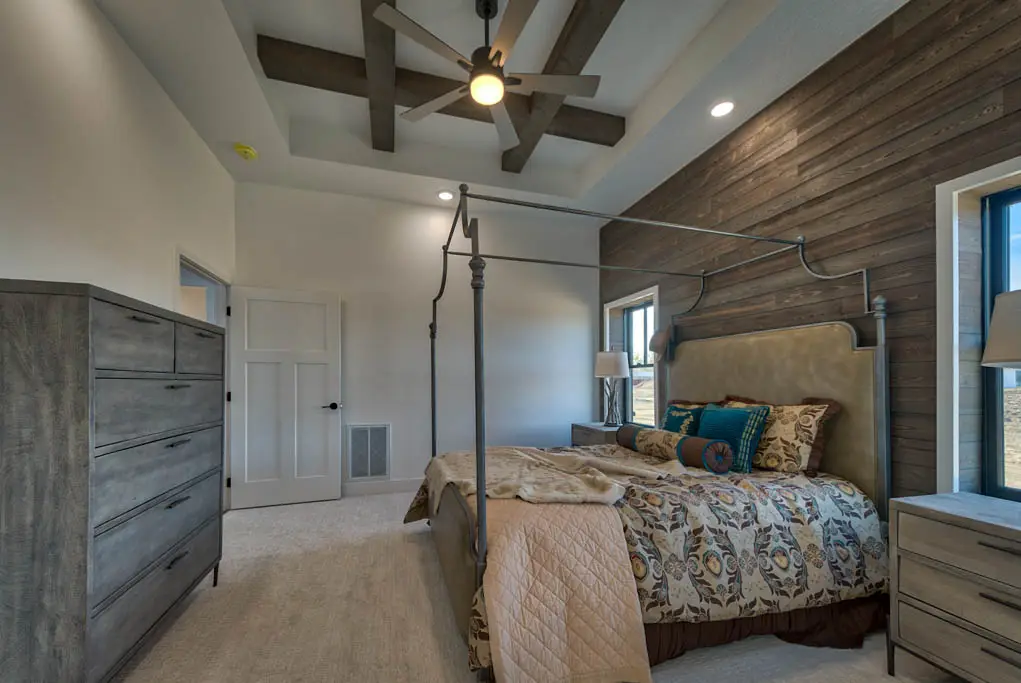 Interior photo of a home built by Harvell Homes in Powell, Wyoming featuring a luxurious and furnished master bedroom with tray and wood-beam ceiling, and floor-to-ceiling shiplap statement wall